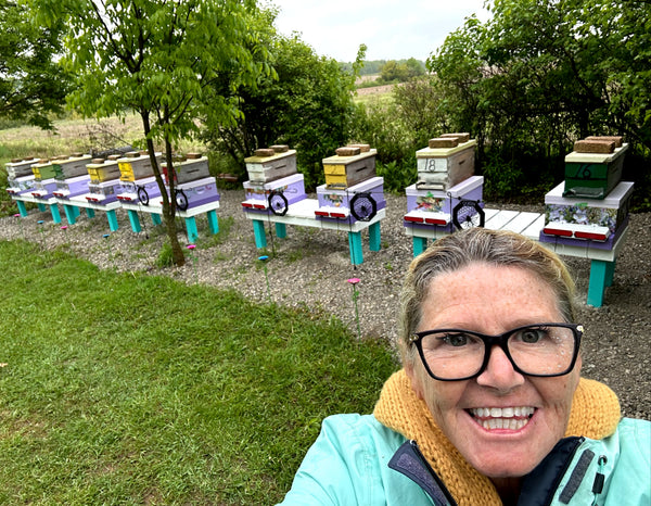Smiling woman takes a selfie at Immersive Honey Bee Experience – Haldimand County, Ontario, with colorful beehives.