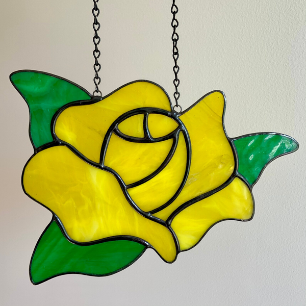 Yellow stained-glass rose pendant with green leaves, suspended by metal chains.